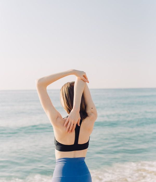 Person feeling energized and stretching outdoors with the sun behind them.
